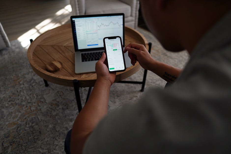 Person trading shares online using a smartphone and laptop on a desk