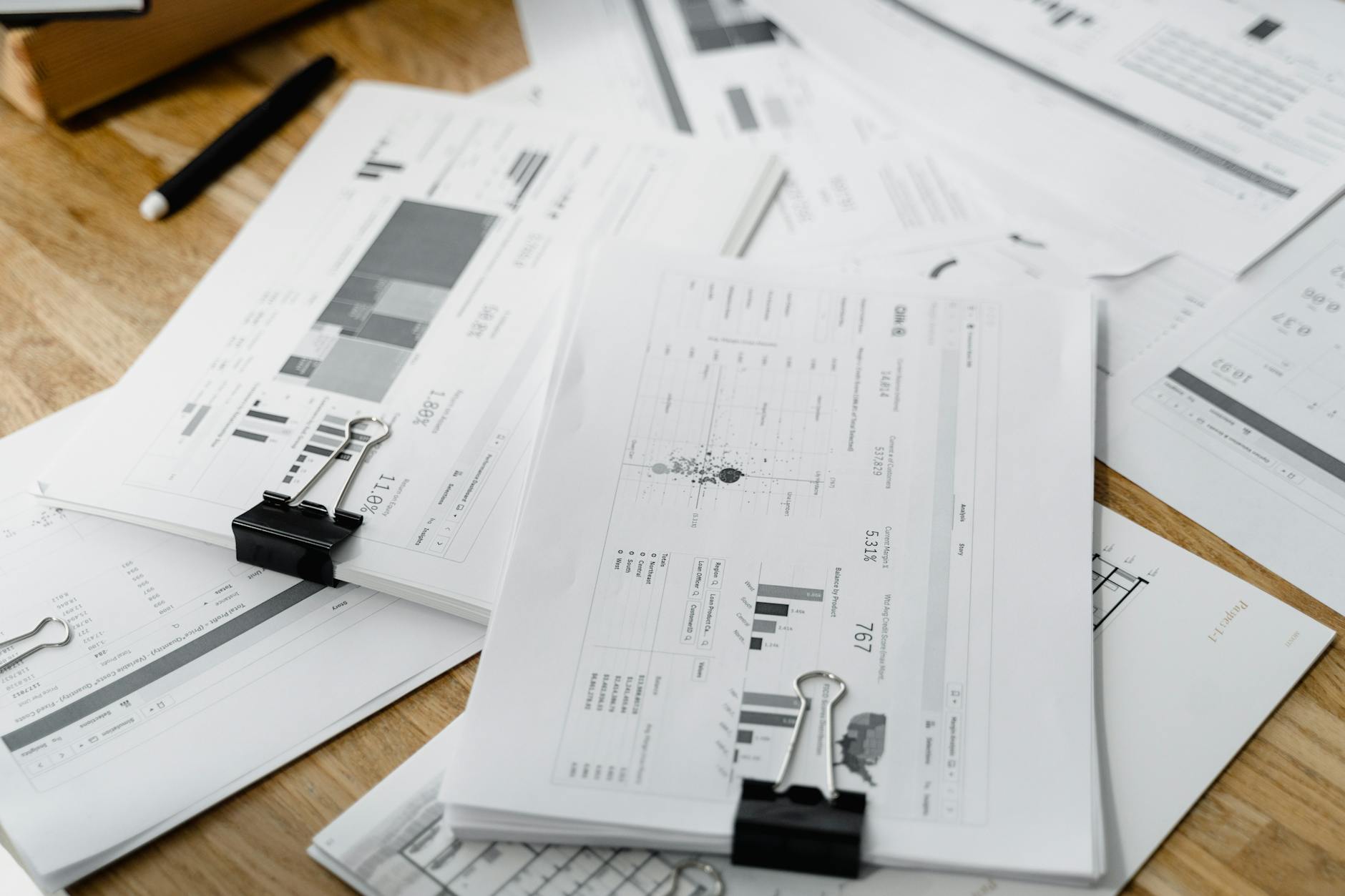 A stack of financial reports and graphs with clips on a wooden desk