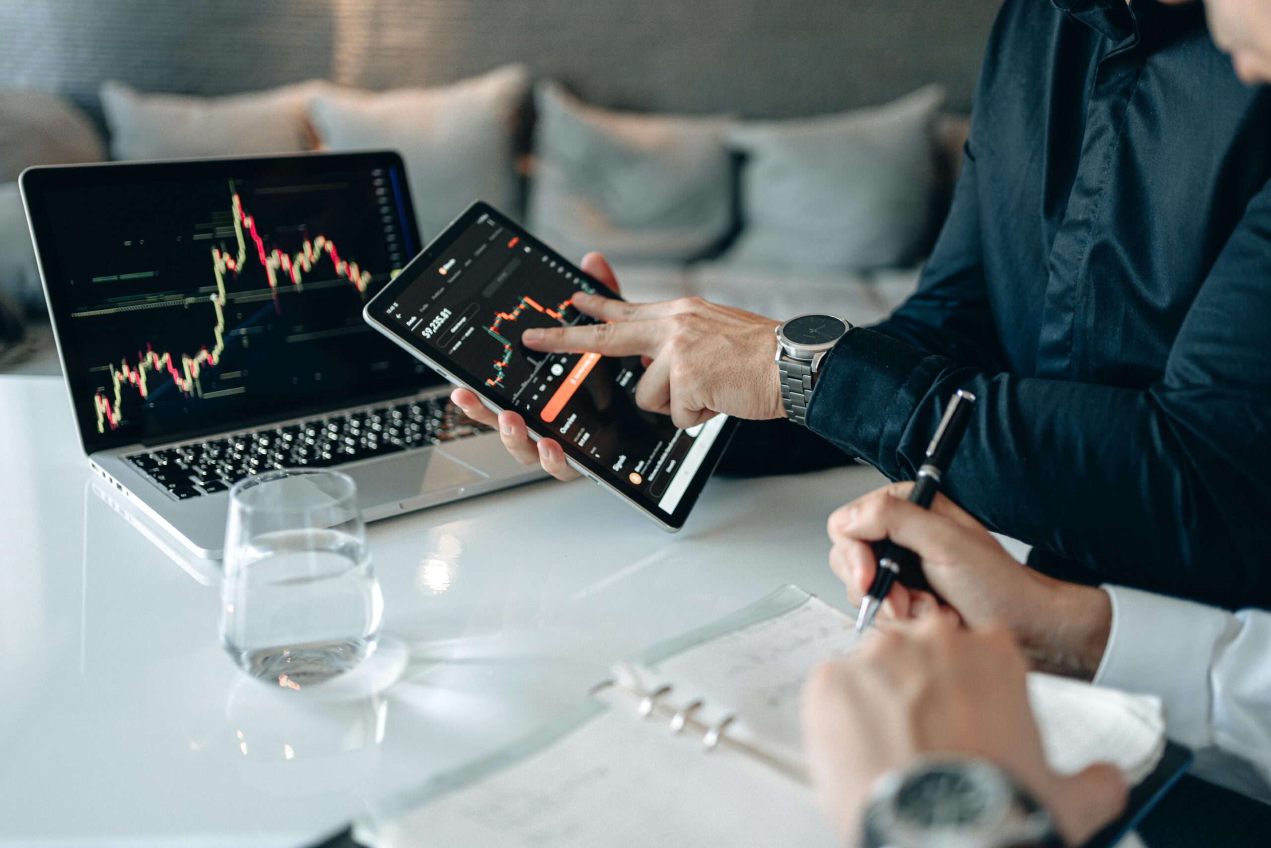 Investors analysing stock charts on a laptop and tablet during a trading discussion