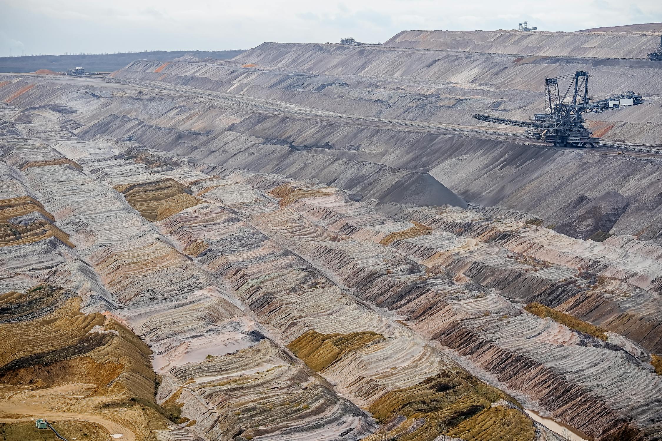 Massive open-pit mine with terraced walls and bucket-wheel excavator