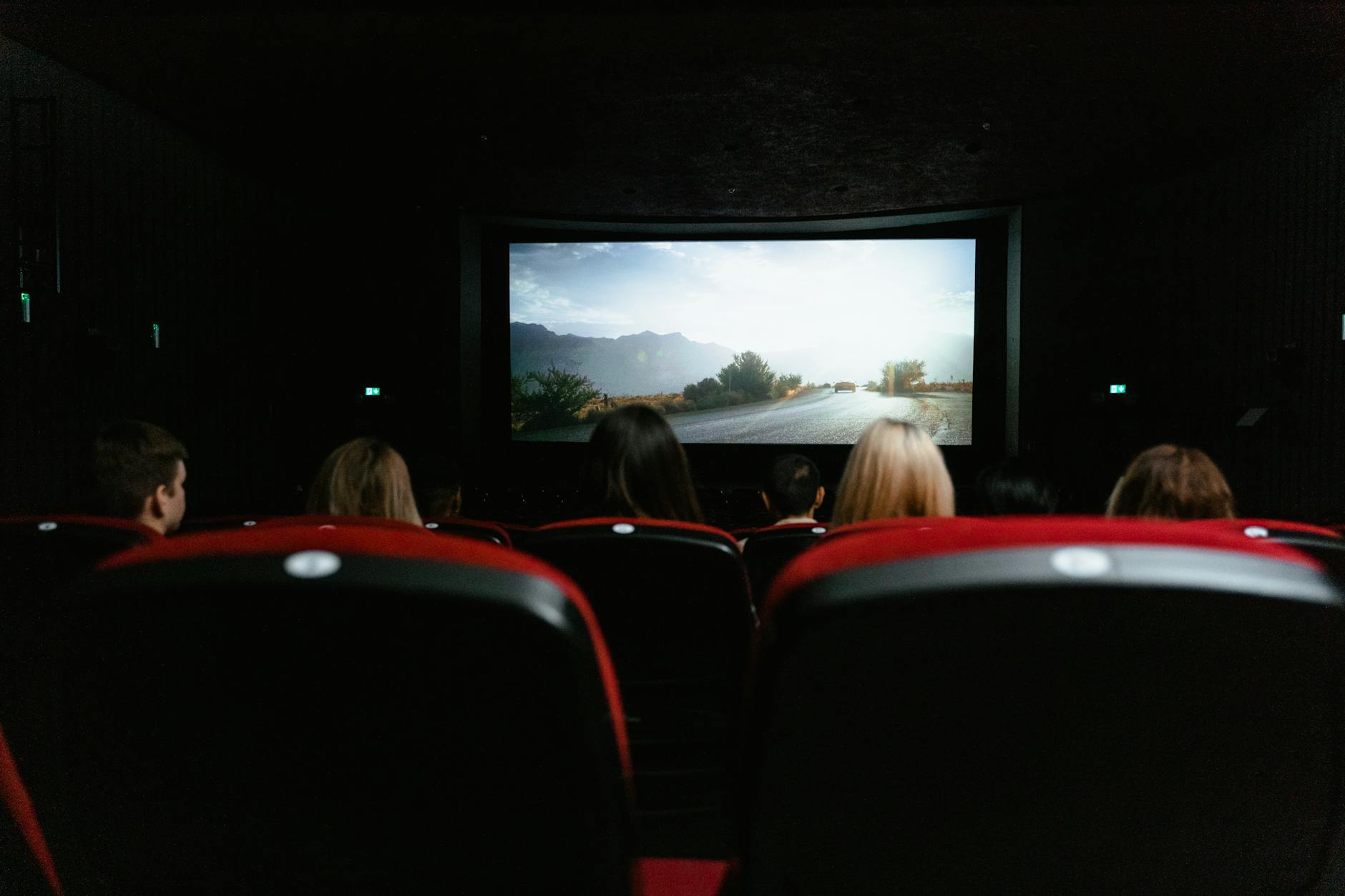 View from behind of people watching a movie in a cinema with red seats and a large screen
