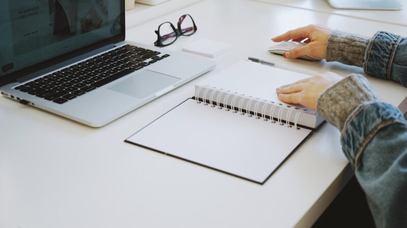Person uses notes and a laptop to check AI draft text before sending it at work