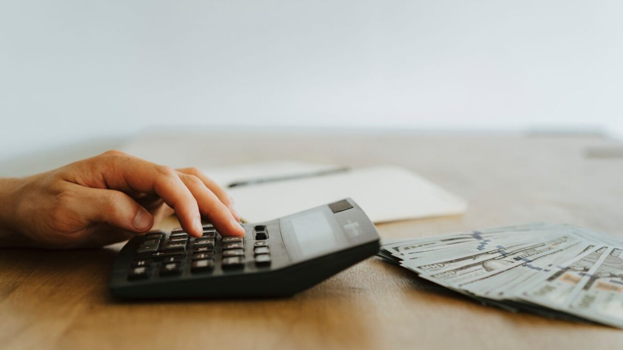 A hand calculating finances with a calculator next to stacks of US dollar bills.
