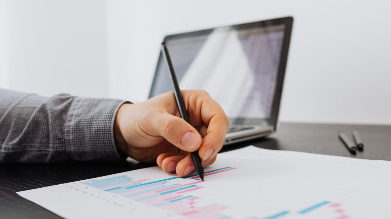 Person taking notes on a business chart with a laptop in the background.