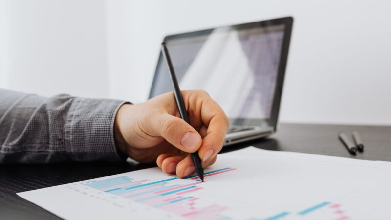 Person taking notes on a business chart with a laptop in the background.
