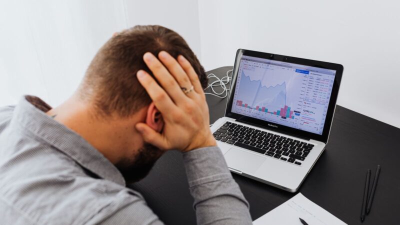 Stressed man at desk looking at declining stock charts during a share suspension, indicating financial loss.