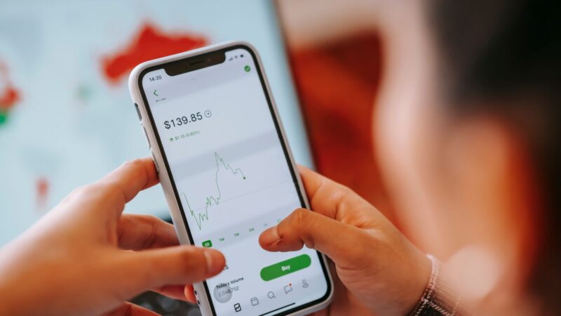 Crop anonymous trader using app on cellphone with graph and dollar price on screen in house