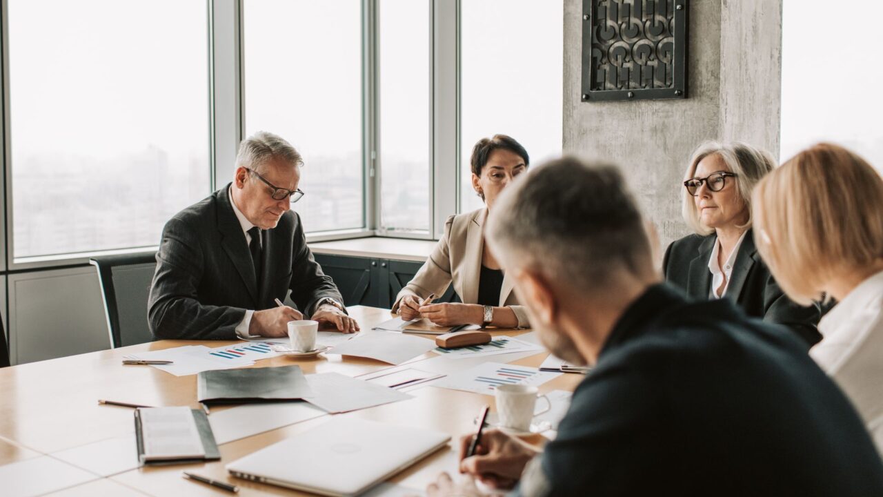 Board members reviewing governance and oversight documents with charts around a conference table