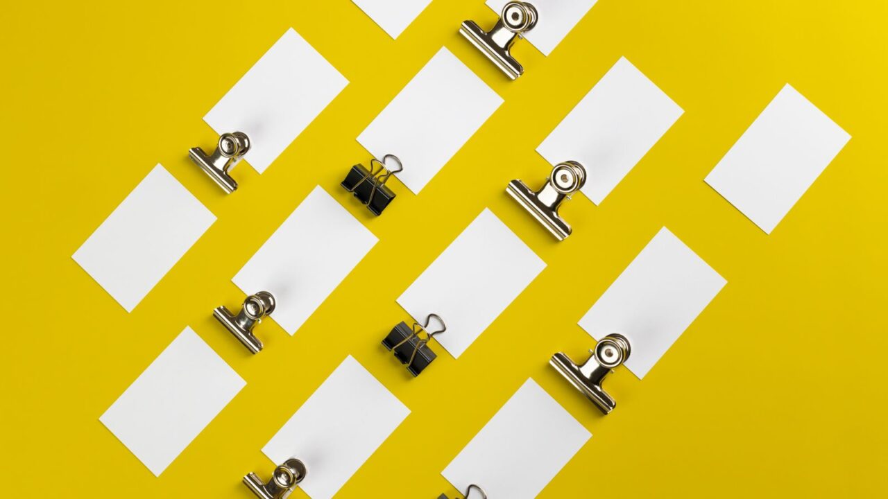 Paper clips and blank cards arranged on a vivid yellow surface.