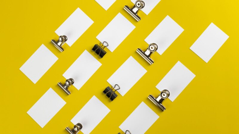 Paper clips and blank cards arranged on a vivid yellow surface.