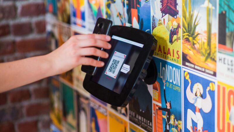 A person holds a smartphone towards a QR code displayed among colourful wall posters.