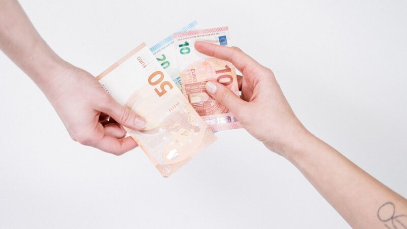Hands passing euro banknotes across a table.
