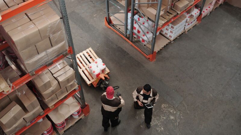 High angle view of warehouse workers organizing inventory with pallets and shelves.