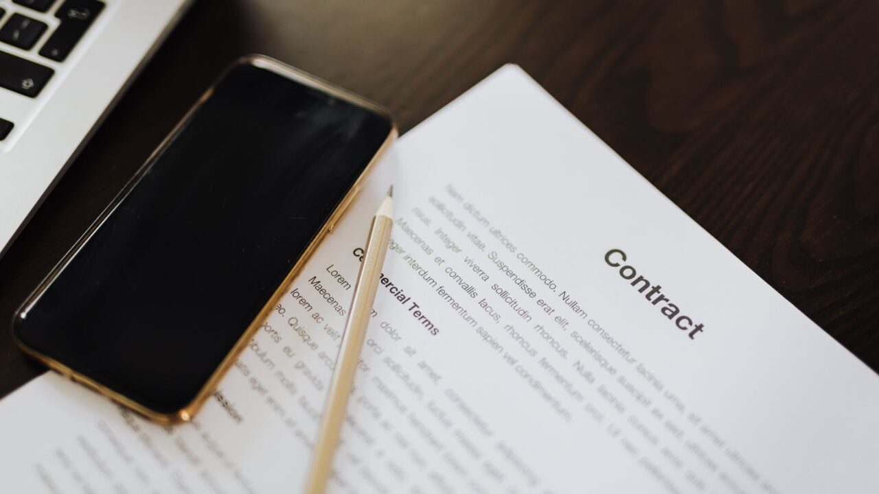 Close-up of a contract document alongside a smartphone and laptop