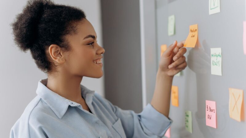 Woman arranging colourful notes on an office whiteboard.