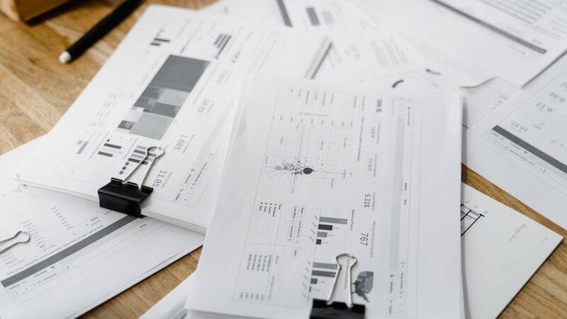 Financial reports with printed graphs held by metal clips on a wooden desk.