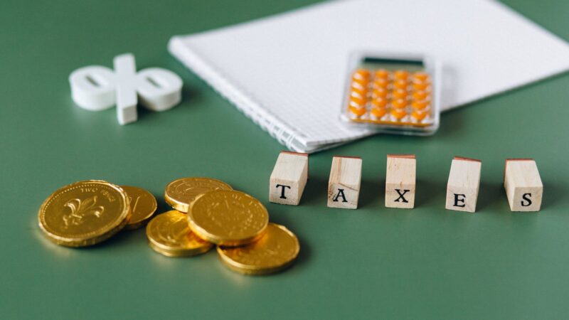 Calculator beside stacked coins and a card marked taxes on a green surface.
