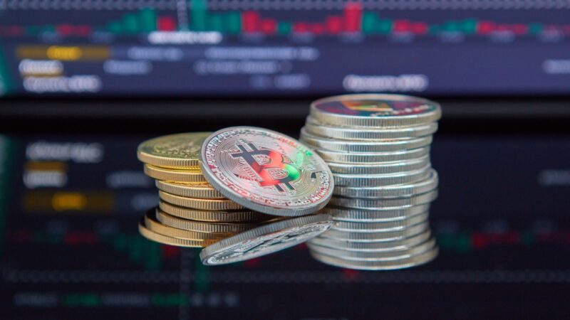 Cryptocurrency coins beside a screen showing a fluctuating market price chart.