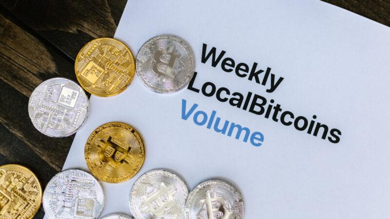 Bitcoin tokens resting on a printed Weekly LocalBitcoins trading-volume chart.